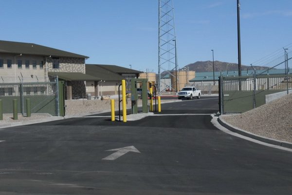 Entry checkpoint to a secure facility with a guard shelter, featuring Delta Scientific high-security yellow bollards in the foreground, ensuring authorized access against a backdrop of rugged mountains.