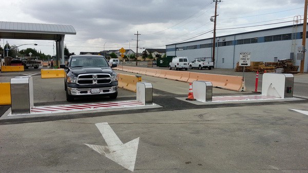 A black pickup truck passing through a Delta Scientific vehicle access control point, featuring a surface-mounted barrier system with striking red and white stripes, under a clear directional arrow indicating the correct route for secure entry.