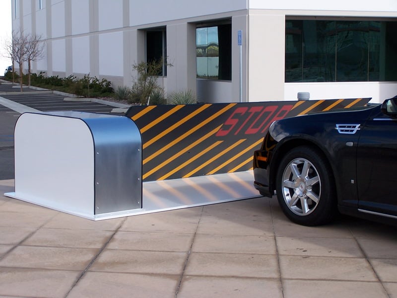 A vehicle approaching a Delta Scientific surface-mounted barrier system with a boldly striped 'STOP' barrier arm, demonstrating the effective use of visual deterrents for secure facility access control.
