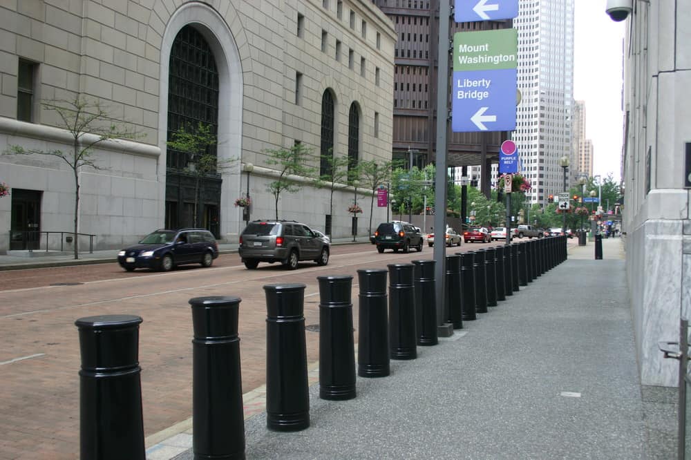 A city sidewalk enhanced with a line of Delta Scientific high-security bollards, providing pedestrian safety along a busy street while seamlessly blending with the urban landscape.