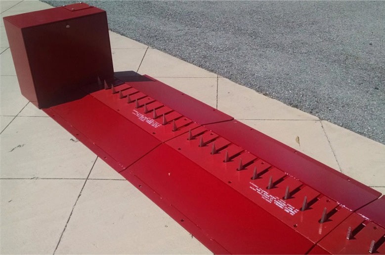 Red flush-mounted Delta Scientific traffic spike system in the engaged position on a concrete surface, designed to enforce one-way traffic control and prevent vehicle intrusion with its sturdy, upward-pointing spikes.