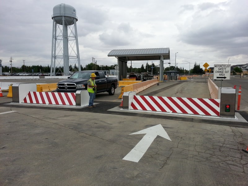 A Delta Scientific mobile counter-terrorist vehicle barricade system in operation at a checkpoint, with a worker in high-visibility clothing for safety, showcasing Delta's capabilities in providing temporary security solutions for checkpoints and sensitive site access control.