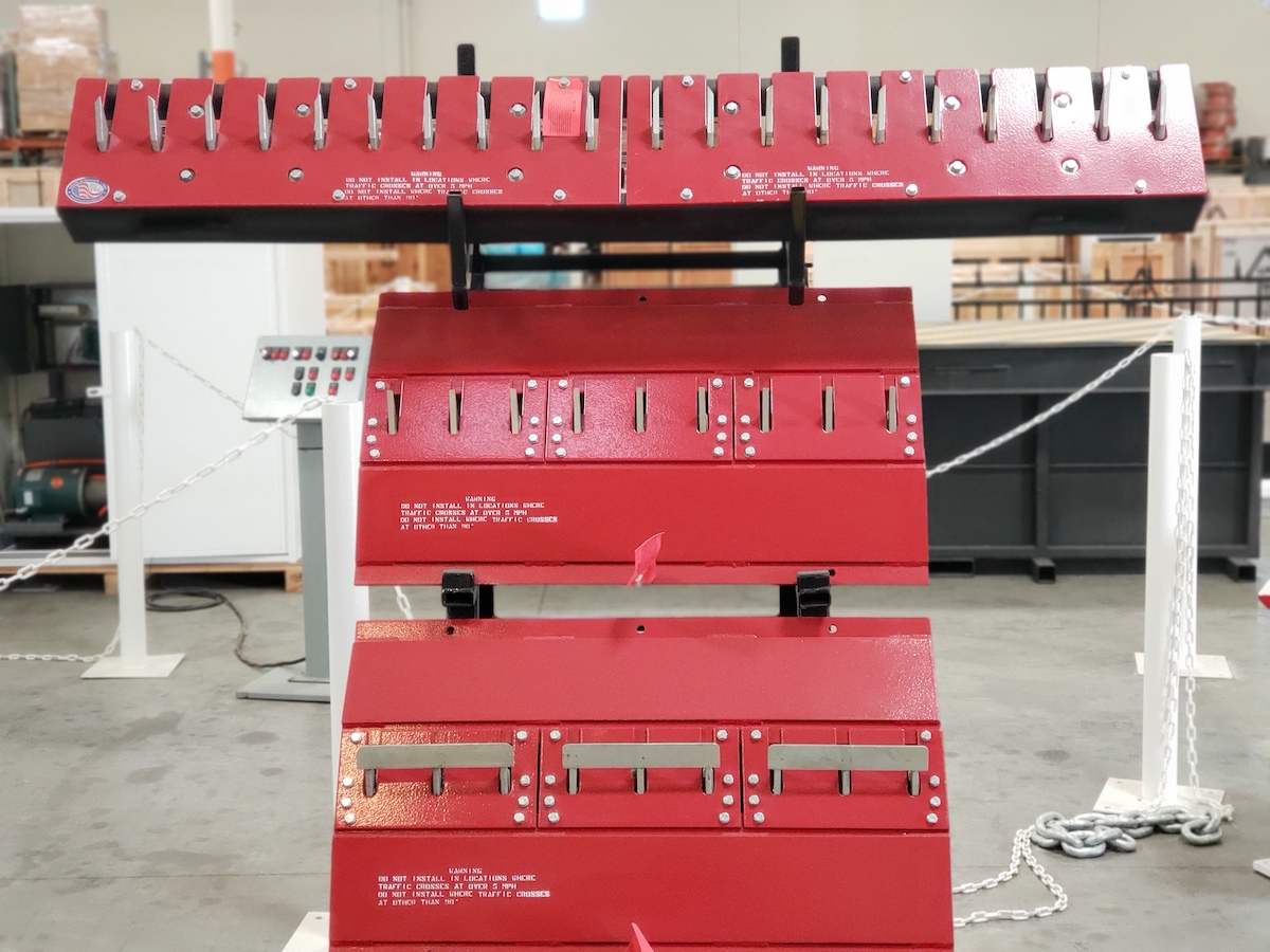 Red motorized Delta Scientific traffic spikes in an inspection setup, showcasing the equipment's retractable teeth designed to regulate vehicle access and ensure secure traffic management in parking and commercial spaces.