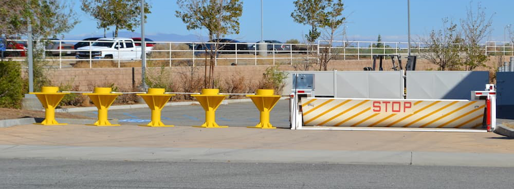Security checkpoint at an industrial facility featuring Delta Scientific yellow bollards and a white barrier arm with bold 'STOP' signage, demonstrating the company’s integrated approach to secure entry control.