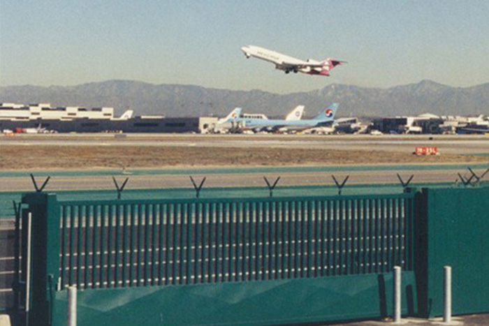 Security gate with anti-climb spikes at an airport, with a jet taking off in the background against a mountainous horizon, representing Delta Scientific's role in airport perimeter security.