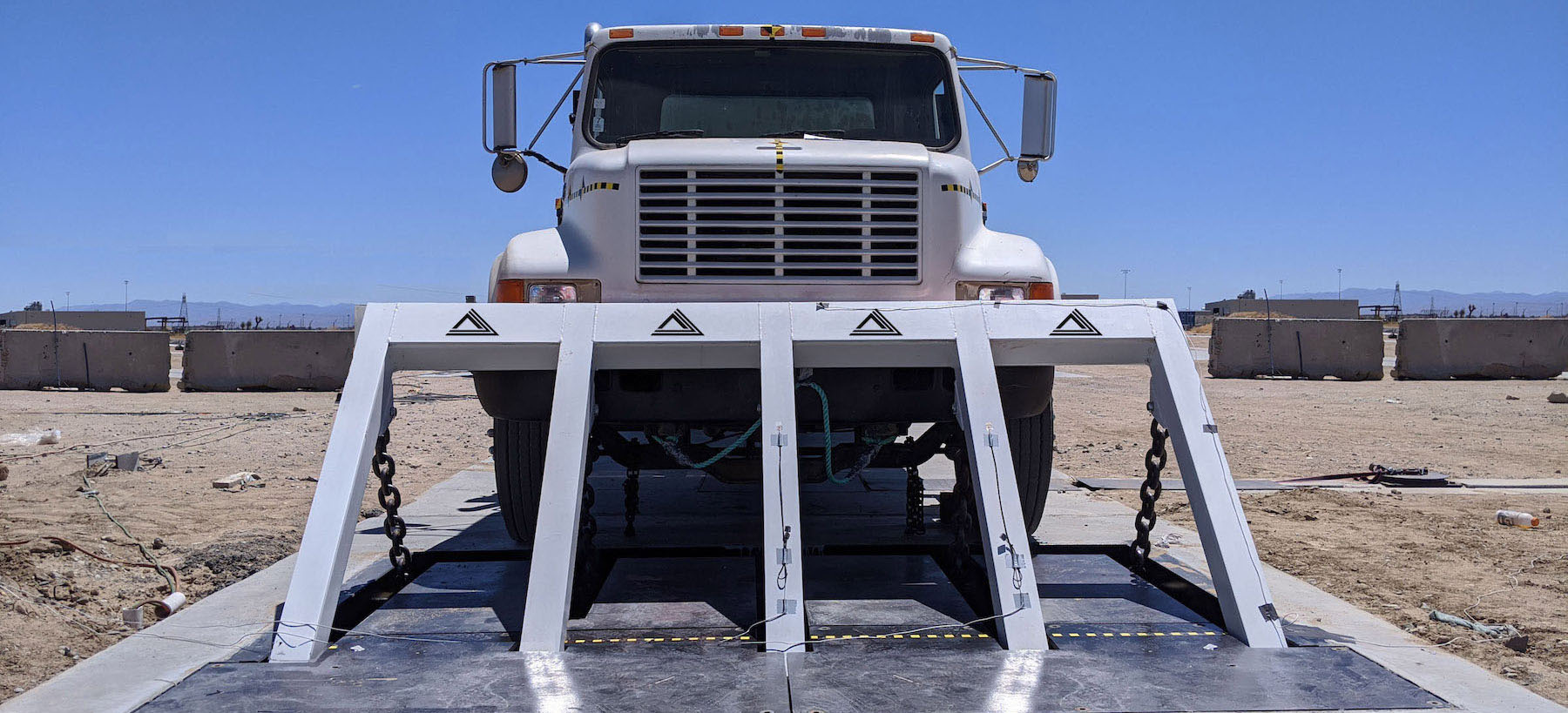 A Delta Scientific crash test in progress, showcasing a heavy-duty vehicle barricade system halting a white truck in a controlled security checkpoint scenario, highlighting the durability and effectiveness of Delta's high-security barriers.