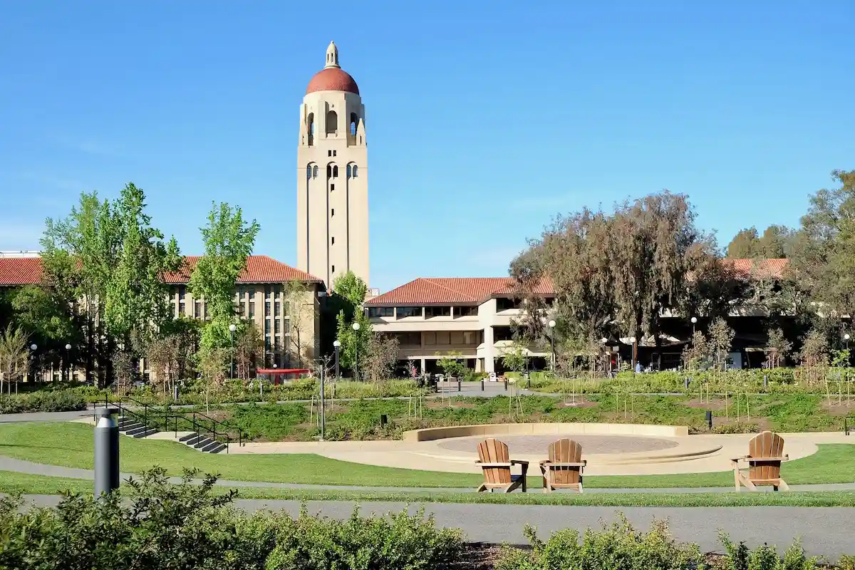 A serene campus environment with the iconic Hoover Tower rising above the university's red-tiled roofs, surrounded by lush greenery and two wooden chairs in the foreground, exemplifying Delta Scientific's commitment to securing educational institutions and maintaining peaceful study spaces.