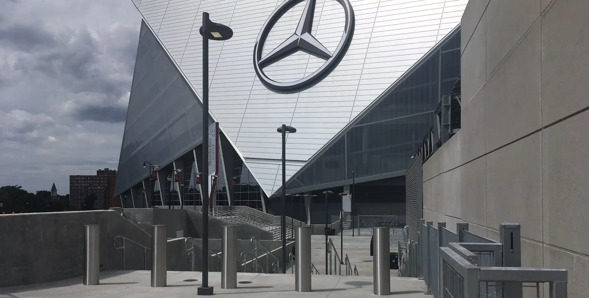 An architectural view of a stadium entrance featuring a large Mercedes-Benz logo, with a row of stainless steel security bollards by Delta Scientific, ensuring a secure yet welcoming pathway for visitors.