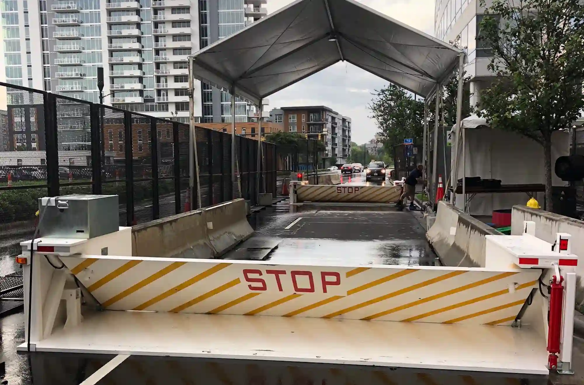 Security checkpoint with Delta Scientific's surface-mounted wedge barriers under a canopy, in an urban setting with modern buildings in the background, ensuring the safety of events and public gatherings.