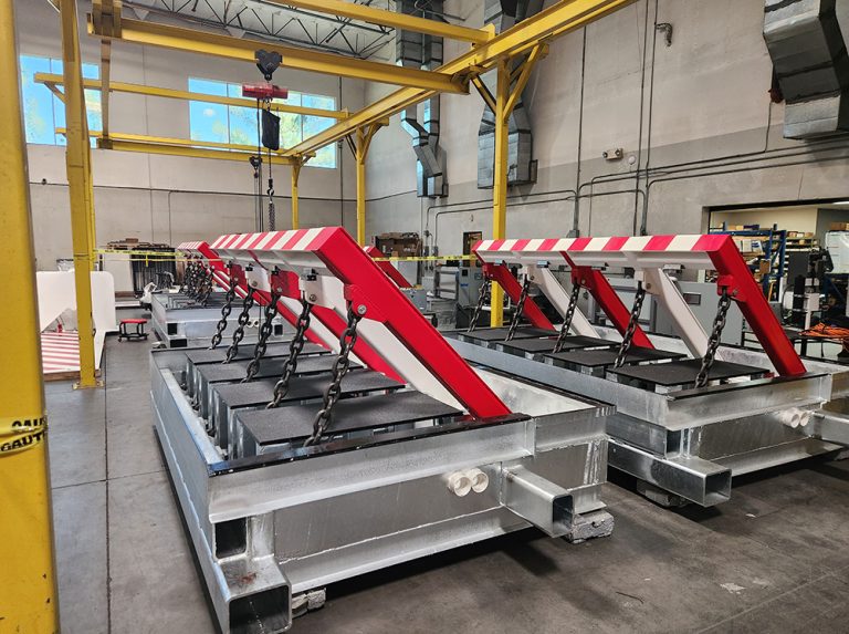 Multiple large crash-rated wedge barriers with red and white stripes are arranged in a spacious industrial warehouse, highlighted by yellow beams overhead.
