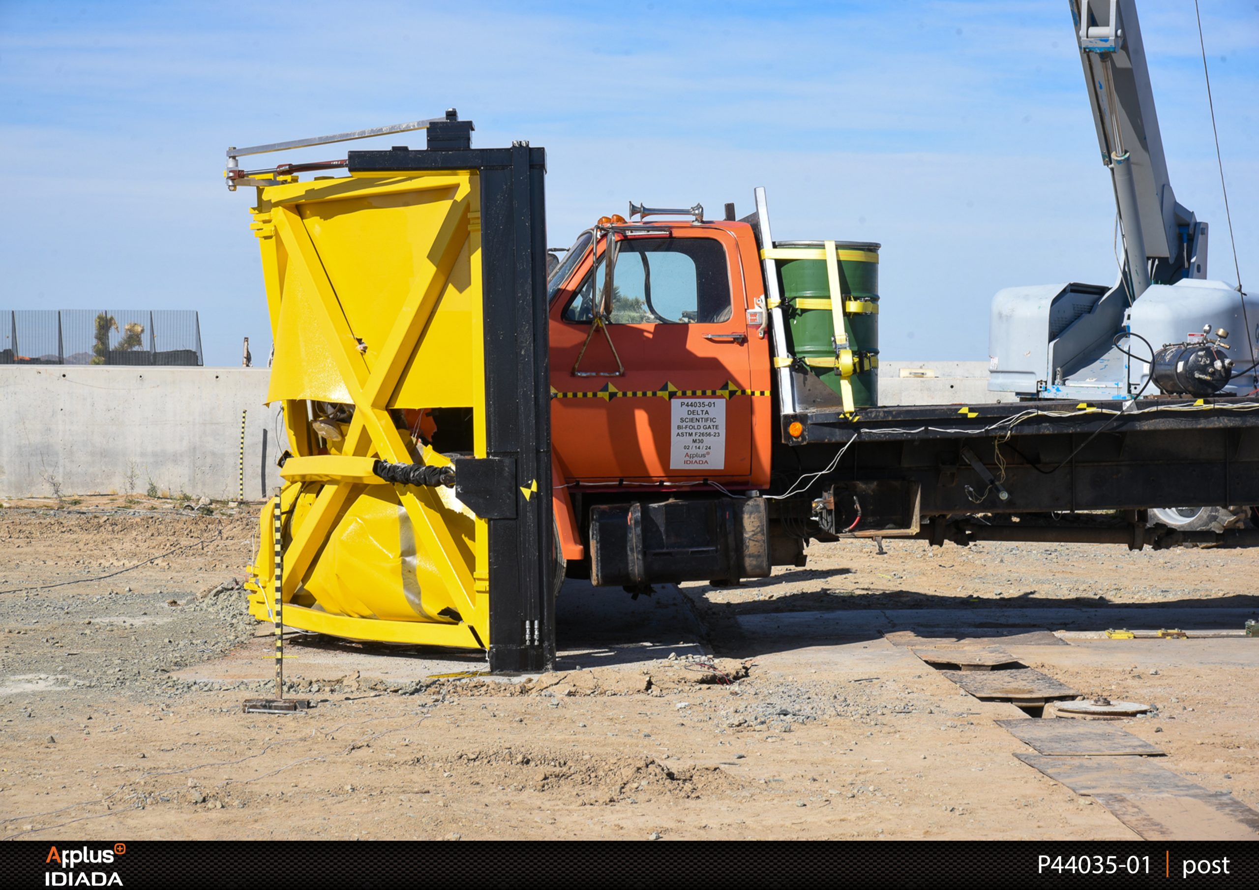 A yellow crash cushion absorbed the impact of an orange truck during a crash test at an outdoor test site featuring a crash rated gate.
