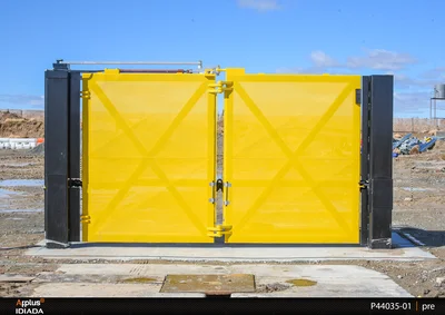 A large yellow crash test barrier with black support columns stands outdoors on a concrete surface at a test facility.