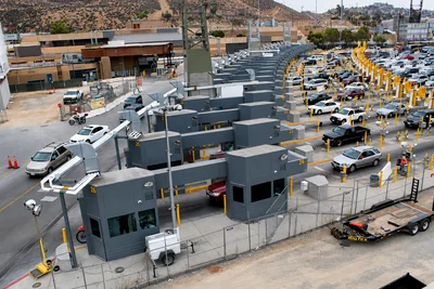 Aerial view of multiple vehicle lanes at a border crossing checkpoint with inspection booths and cars waiting in line.