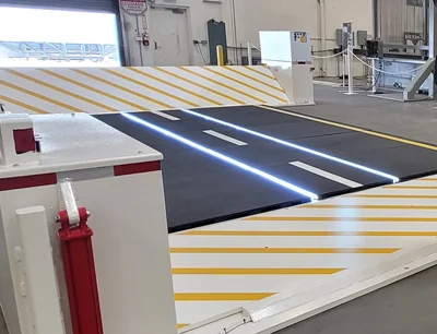 A retractable security barrier with yellow stripes and LED road markings is installed inside an industrial facility.