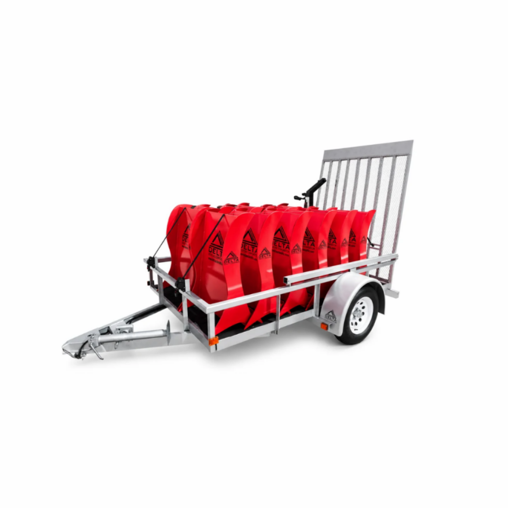 A metal trailer carrying several red plastic water barriers, shown on a white background.