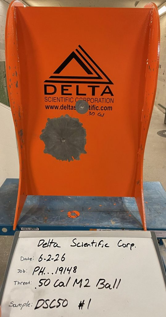 Orange Delta Scientific steel plate with a large bullet impact in the center, the result of rigorous ballistic testing. A label below details the test date, job, threat type (.50 Cal M2 Ball), UL 752 Level 9, sample number (DSC50 #1), and DSC50BR specification.